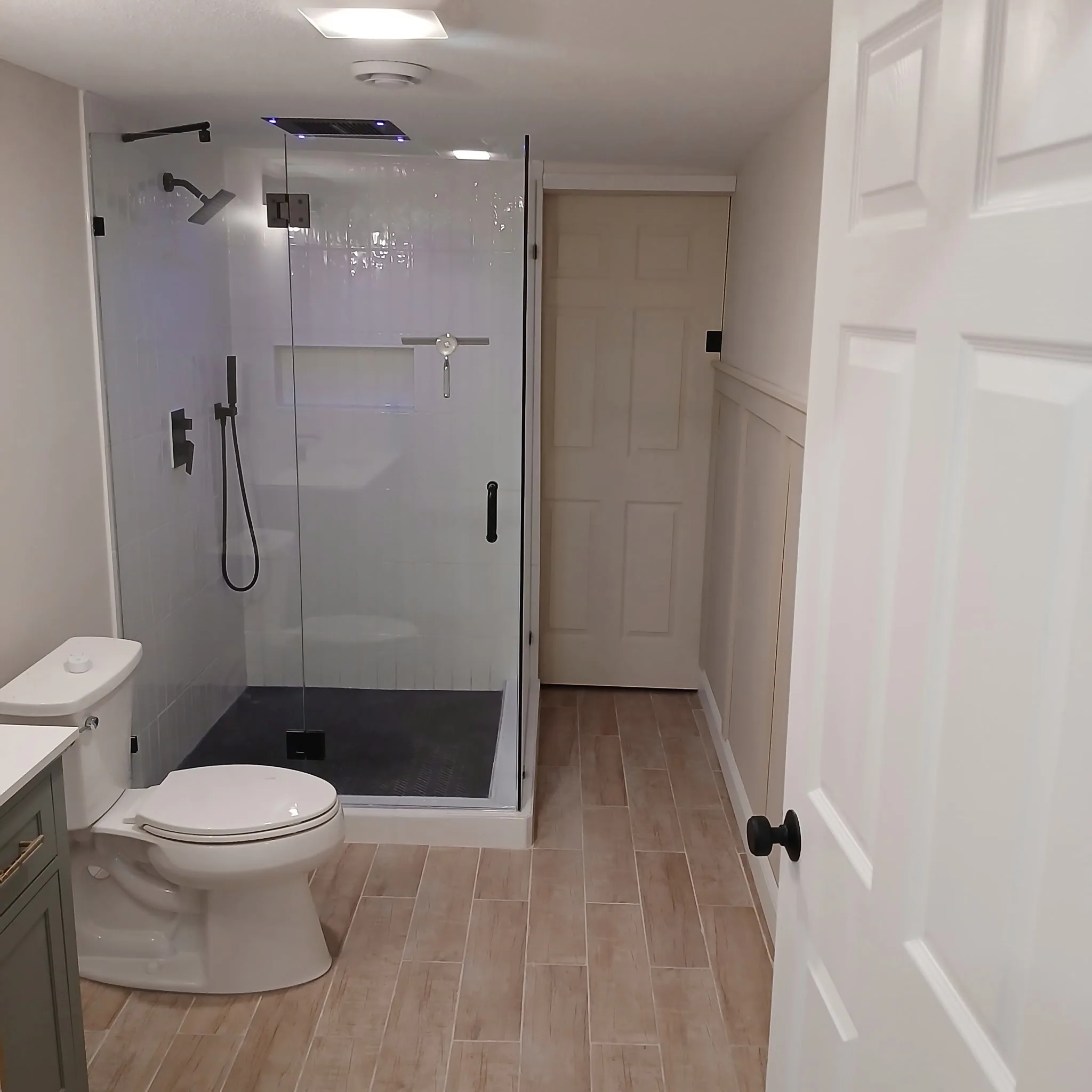 Finished bathroom remodel with tiled walk-in shower, glass enclosure, and wood-look tile floor